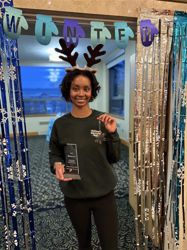 image of girl ( Torrie Boykins) smiling holding Award for Holiday Harmony Bash received the 2025 Outstanding Collaborative Program Award from the Association of College Unions International and a clear snowflake tree ornament